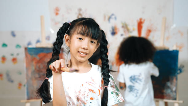 istock Creative girl pose at camera while diverse children painting behind. Erudition. 2152011054