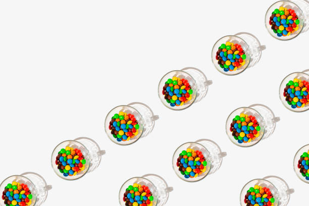 Pattern made of drinking glass full of multicolored candies on a white background with copy space.