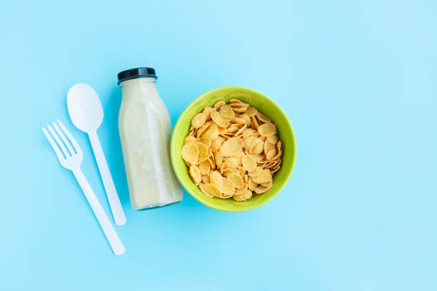 Corn flakes in green bowl with spoon, fork and milk on blue background, Breakfast cereal