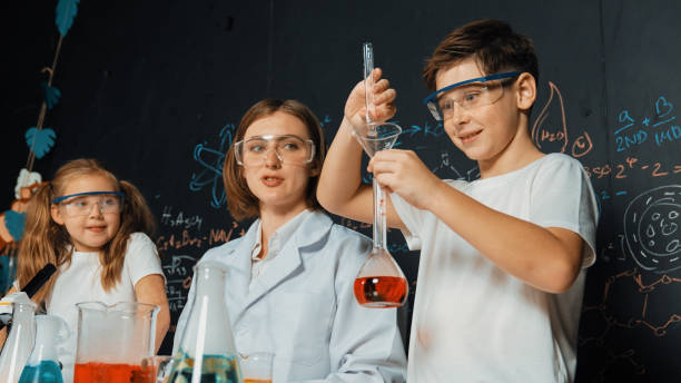 istock Caucasian boy mixing chemical liquid while teacher giving advice. Erudition. 2152014267