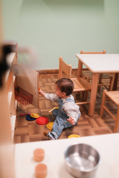 A cheerful baby crawls on the floor of a playroom. Two mothers are in the background, engaging with babies, promoting an interactive and nurturing environment. The scene conveys joy, learning, and social interaction.