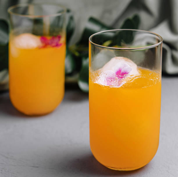 Refreshing orange cocktail with floral ice cubes Elegant orange drinks with edible flowers in ice, perfect for summer events martini glass flower arrangement stock pictures, royalty-free photos & images