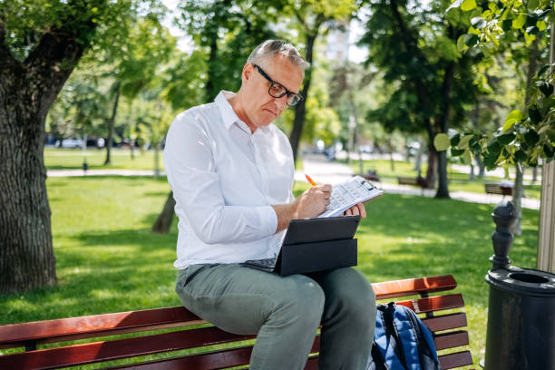 istock Man working in public park using digital tablet while sitting on park bench and writing something 2152024454
