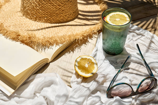 istock Reading during summer holidays. Book, rifresh drink, sunglasses and hat on white beach blanket on wicker chair in tropical garden. Summertime mood. 2152029072