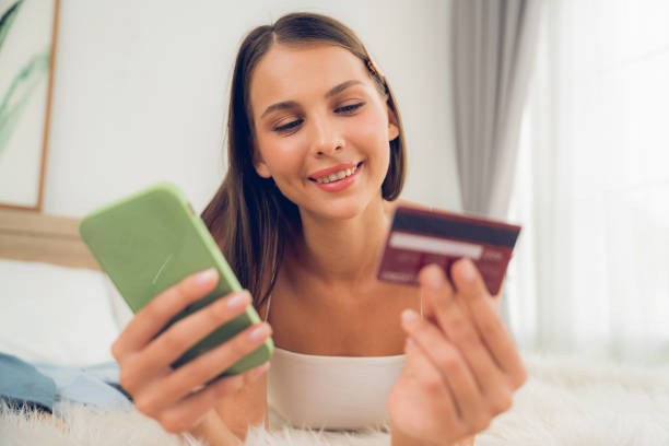 istock Young woman lying on bed using online payment app. Unveiling 2152036734