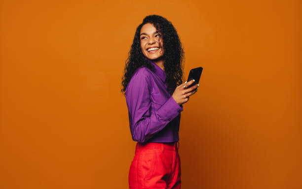 istock Cheerful woman using vibrant mobile phone against orange background 2152039549