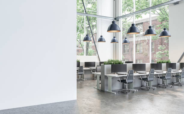 Side view of a semi-empty office interior with white wall and copy space,  work desks and large windows  on concrete floor