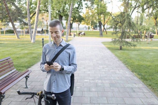 istock Smiling businessman commuter using mobile phone. He is enjoying at public park on his bicycle trip from work after a long workday. Sustainable concept of going to work by an electric bicycle 2152039994