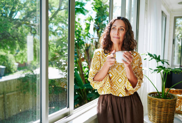 istock Mature woman looking out of a window at home while drinking coffee 2152059873