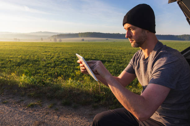 Man, traveler resting using tablet when sitting in car with spring fog Czech landscape