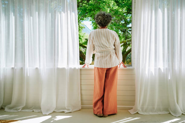 istock Mature woman looking out through a window at home 2152060816