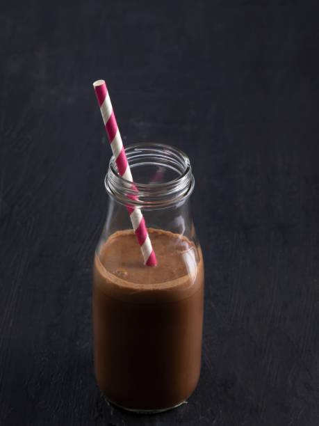 Chocolate drinks in glass bottles with paper straw on neutral background