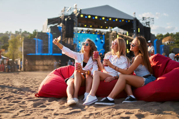 istock Three women relax on red bean bag chairs at beachfront music event, enjoying drinks, sunny weather. Group takes selfie, smiles, surrounded by festival atmosphere, upbeat crowd, ocean backdrop. 2152070591