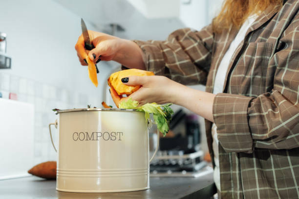 istock Compost the kitchen waste, recycling at home. Compost bin with vegetables cutted leftovers on the kitchen table with blurred woman cooking meal. Environmentally responsible, ecology. Selective focus 2152075408