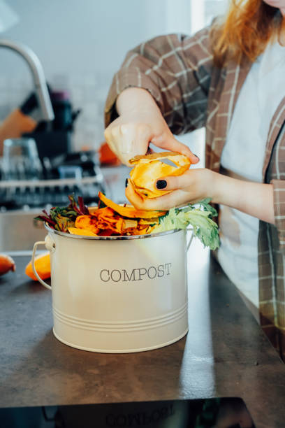 istock Compost the kitchen waste, recycling at home. Compost bin with vegetables cutted leftovers on the kitchen table with blurred woman cooking meal. Environmentally responsible, ecology. Selective focus 2152075415