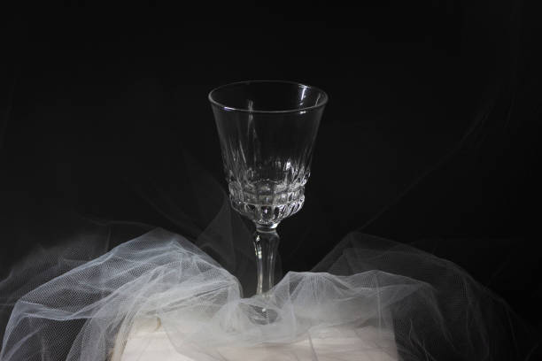 istock Empty wine glass on a white tulle in front of a black gackground. Soft illumination. 2152077190