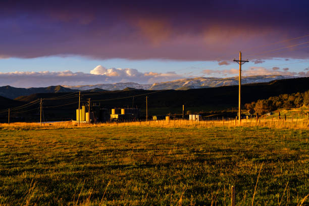 Oil and Gas Development in Rural Area - Gas tanks used for natural gas energy development in agricultural field in rural ranching area. Scenic views of mountains and dramatic sky during golden hour sunset.