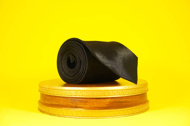 istock Plain fabric black necktie rolled on display board with yellow color background close-up view single object 2152089948