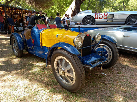 San Isidro, Argentina - Oct 7, 2022: Old blue and yellow 1920s Bugatti racecar on the lawn under the trees at a classic car show.