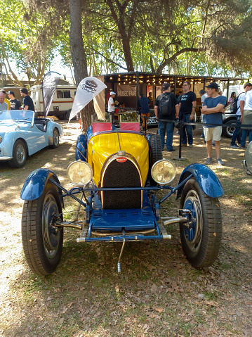 San Isidro, Argentina - Oct 7, 2022: Old blue and yellow 1920s Bugatti racecar on the lawn under the trees at a classic car show. Front view. Copy space