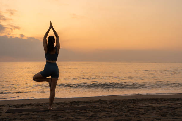 istock lady doing the tree pose at the beach. sunrise yoga 2152099143