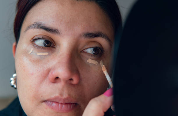 istock young latina woman applying concealer while looking in the mirror 2152104114