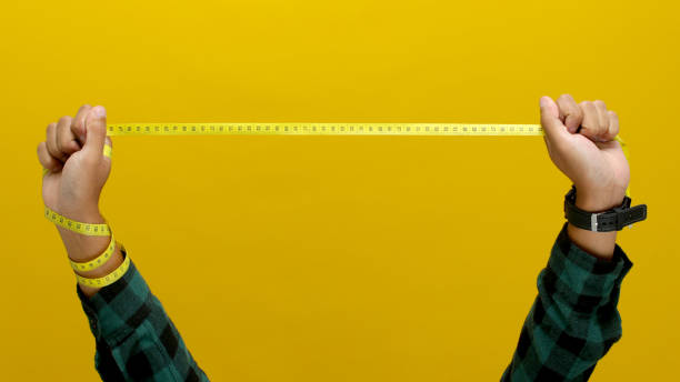 istock Hand holding a measuring tape against a yellow background 2152114362