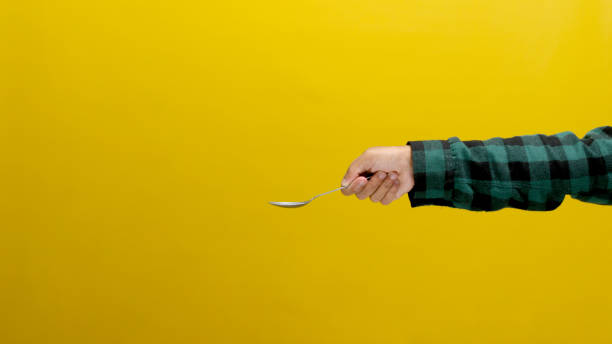 istock Hand Holding a Silver Stainless Steel Spoon on Yellow Background 2152115542
