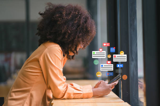 smiling african american businesswoman engaging with social media on smartphone at modern workspace. - sociala-medier bildbanksfoton och bilder