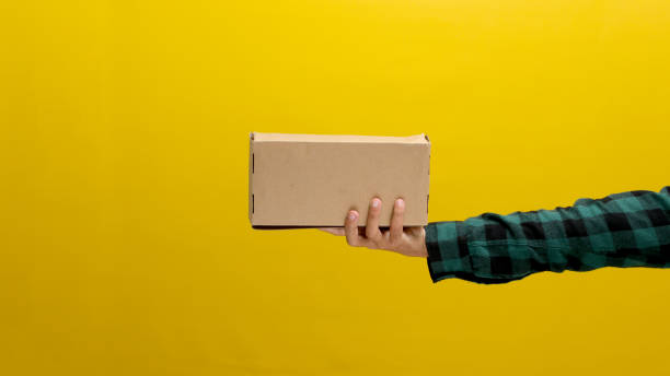 istock Hand holding a cardboard box against a yellow background 2152118322