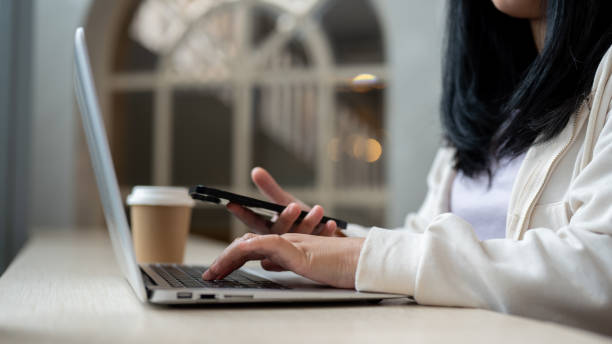 istock A cropped image of an Asian woman using a smartphone and laptop computer, working remotely at a cafe 2152120078