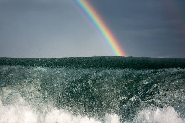 Wave breaking under a distant rainbow with dark skies