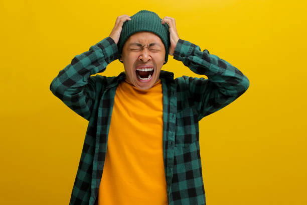 istock Frustrated young Asian man is screaming while holding his head, appearing panicked, and scared 2152126318