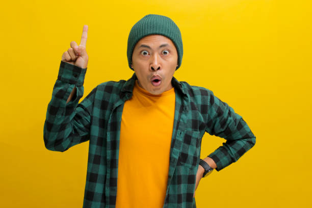 istock Surprised young Asian man is pointing his finger up at an empty copy space 2152135588