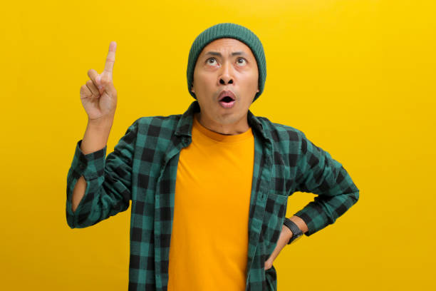 istock Surprised young Asian man is pointing his finger up at an empty copy space 2152135800
