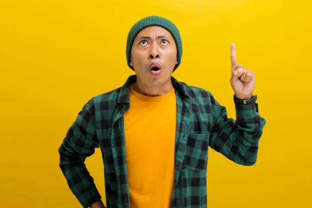 istock Surprised young Asian man is pointing his finger up at an empty copy space 2152135853