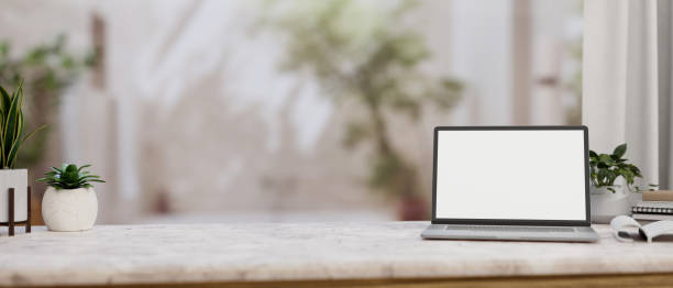 istock A white marble tabletop features a white-screen laptop computer mockup in a room with an indoor tree 2152138236