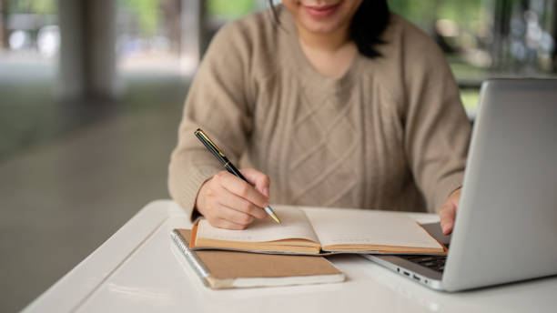 istock A cropped image of an Asian woman taking notes in her notebook while working on her laptop computer. 2152139067