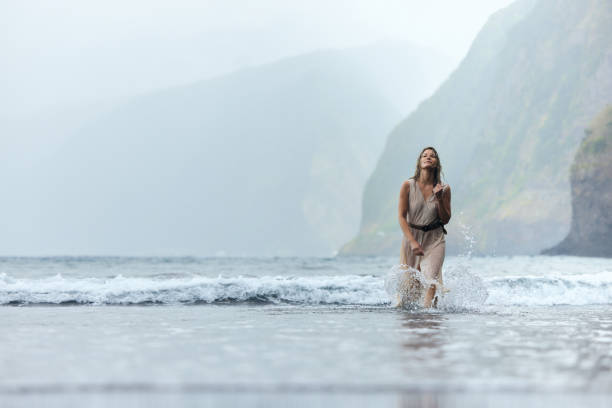 Young carefree woman walking through sea during rainy day on the beach. Copy space.