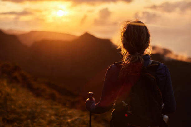 Back view of a female backpacker looking at sunset view from a mountain.