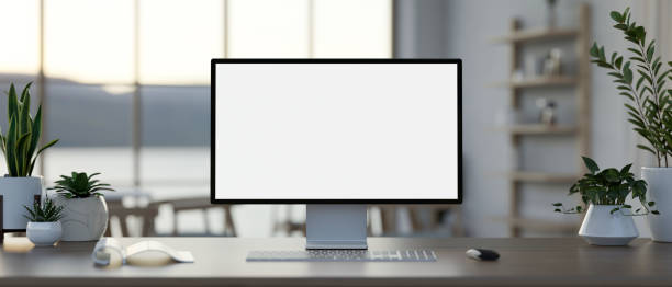 A computer desk in a modern co-working space feature a white-screen computer mockup. A close-up image of a computer desk in a modern co-working space features a white-screen computer mockup, a keyboard, and potted plants. place of work concept. 3d render, 3d illustration desktop pc stock pictures, royalty-free photos & images