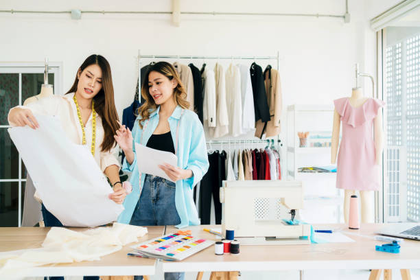 istock Asian female fashion designer or tailor with assistance preparing cut paper fabric pattern. Dressmaker working and designing new fashion collections for customers in atelier tailor workshop. 2152140979