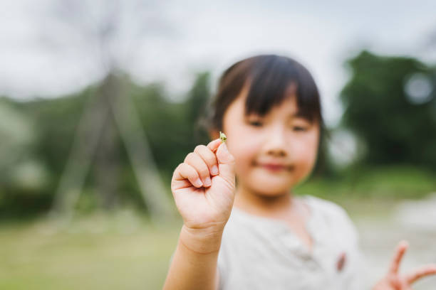 Artistic black and white photo of a young girl standing on a playground slide, wearing a striped hat with a flower. The child looks pensively at the camera, captured in natural light. Concept of childhood emotion, nostalgia, innocence, and timeless moments.