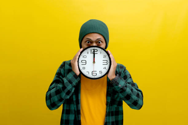 istock an Asian man holds a clock in front of his face, looking at the camera with a surprised expression 2152143349