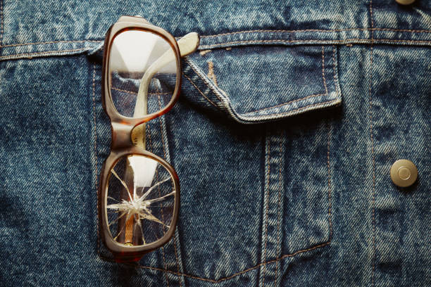 Damaged broken eyeglasses attached to the pocket of denim jacket