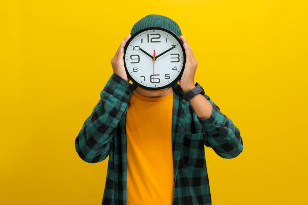 istock Asian man uses a clock to cover his head or face, while standing against a yellow background 2152148647