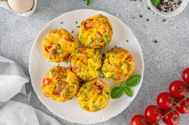 istock Egg muffins or egg bites with bacon, cheese, vegetables and herbs on a white plate on a concrete background. Healthy breakfast. 2152150097
