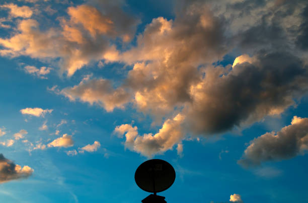 silhouette of a satellite dish against a cloudy sky at sunset