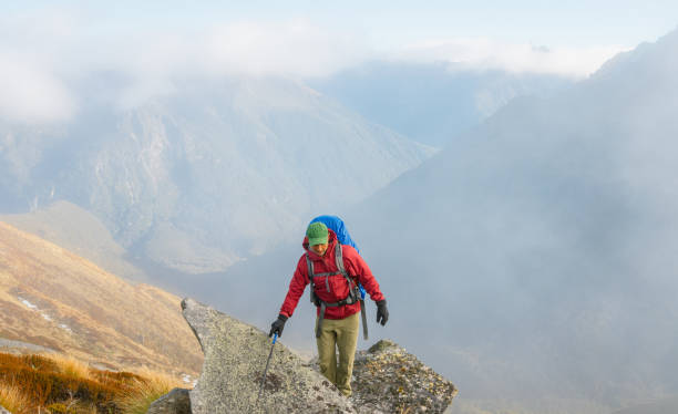 Mountain hiking man / person on summit with panorama view over landscape, peaks, alps and a foggy dale. Sunbeams from sun backlit.
