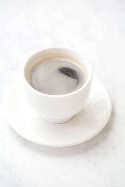 A cup of coffee with saucer rests on a clean white table.
